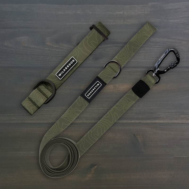 Olive Waterproof Pro Leash + Collar Bundle with topographic pattern, metal hardware, and black branded tags on wood.
