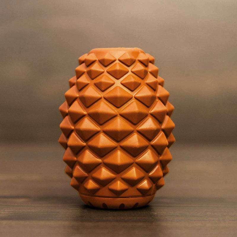 The Conifur, a brown oval interactive dog toy with a geometric, pyramid-textured surface, stands upright on a wooden surface against a blurred background.
