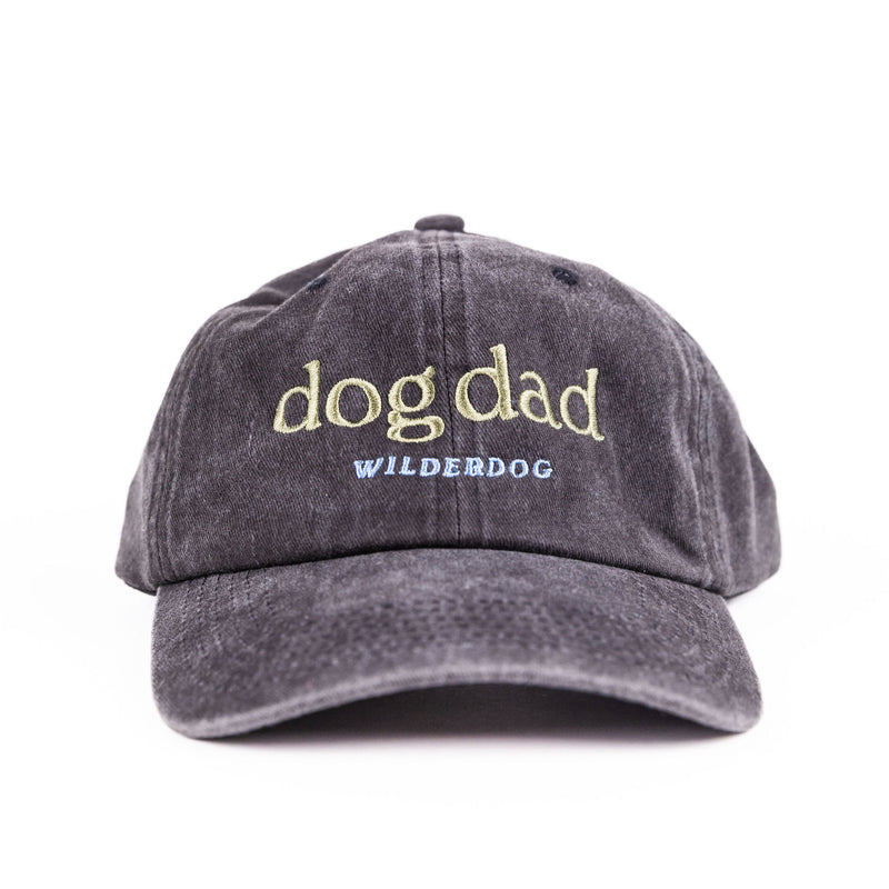 The Dog Dad Hat is a dark gray baseball cap featuring "dog dad" embroidered in yellow and "WILDERDOG" in blue on the front, displayed against a white background.