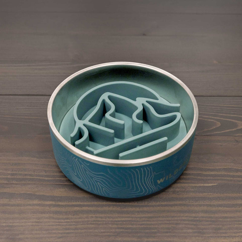 A Silicone Slow Feeder Insert, teal-colored and dishwasher safe, sits in a stainless steel dog bowl on a dark wooden surface, combining the durability of steel bowls with the slow feeding benefits of silicone.