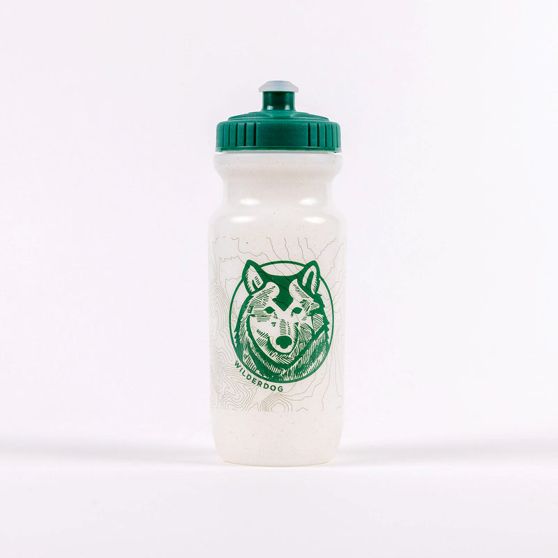 The Plant-Based Water Bottle is a white bottle with a green cap, adorned with a green graphic design of a dog's face on the front. The word "WILDERDOG" is positioned below the dog's face, and the environmentally friendly bottle showcases a topographical map pattern in the background.
