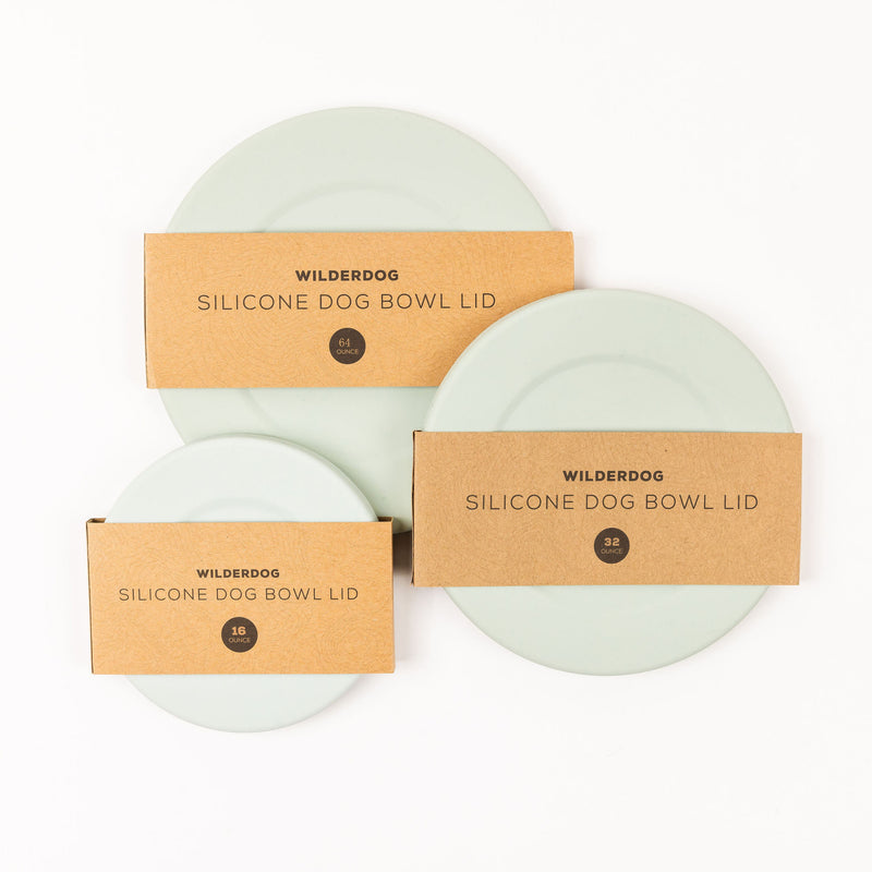 Three light green, food-grade Silicone Bowl Lids in sizes 4.1, 7.2, and 16 come packaged in cardboard sleeves labeled "Wilderdog Silicone Dog Bowl Lid." These dishwasher-safe lids are arranged flat on a white background, showcasing the front packaging.