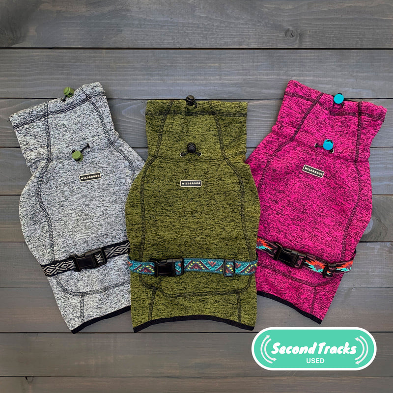 Three (Used) Fleece Jackets for dogs in gray, green, and pink are arranged side by side on a wooden surface. Each jacket has an adjustable strap with a clip. The “Second Tracks Used” logo is in the lower right corner.
