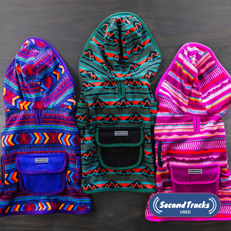Three (Used) Patterned Fleece Jackets made from soft, low-pile fleece with colorful patterns and front pouches are laid side by side on a dark surface. The "Second Tracks Used" logo is visible in the lower right corner.