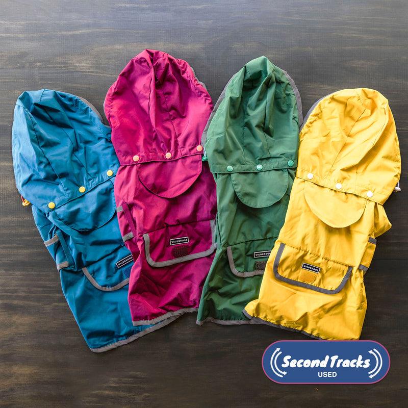 Four (Used) Rain Jackets—blue, pink, green, and a surprise color—are lined up on a wooden surface. The "Second Tracks USED" logo is displayed in the lower right corner.