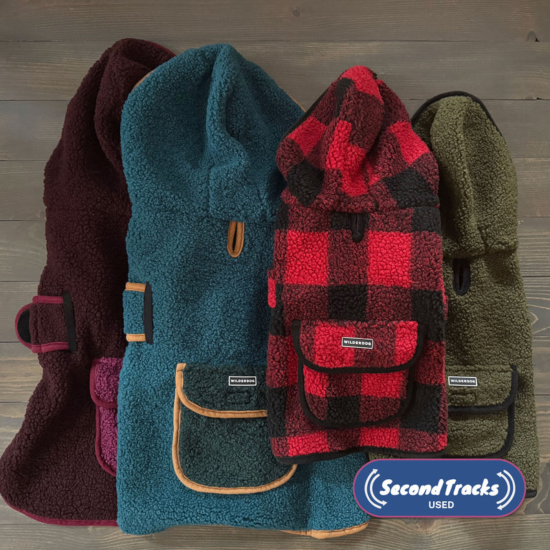 Four (Used) Sherpa Jacket / Shacket dog jackets—burgundy, teal, red plaid, and a mystery color—are arranged side by side on wood. A "Second Tracks USED" logo is in the corner. Perfect for cozy dog apparel fans!.