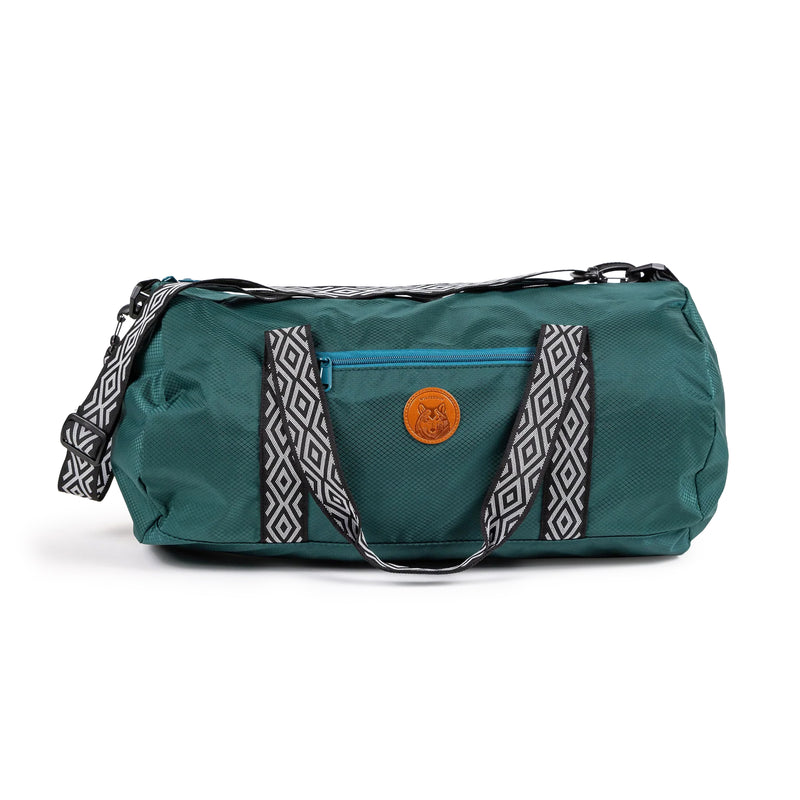 Dog Duffel in teal with black-and-white straps, blue zipper pocket, and a round leather patch on the front.
