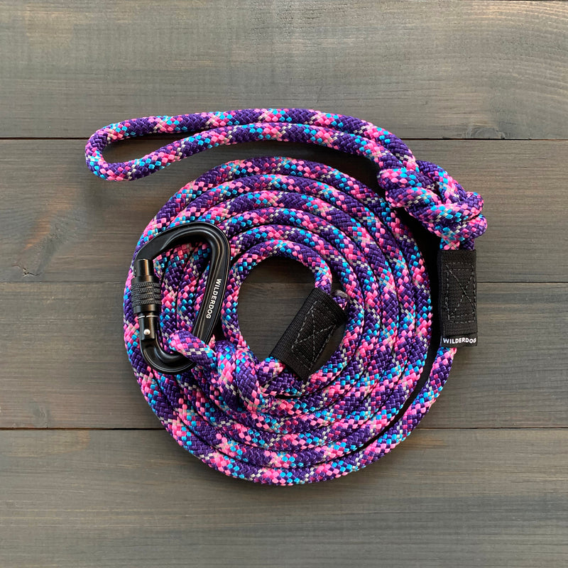 The Razzleberry Reflective Leash is a coiled, multi-colored, durable dog leash equipped with a black carabiner clip at one end. The leash boasts an intricate pattern of purple, pink, blue, and white. It&