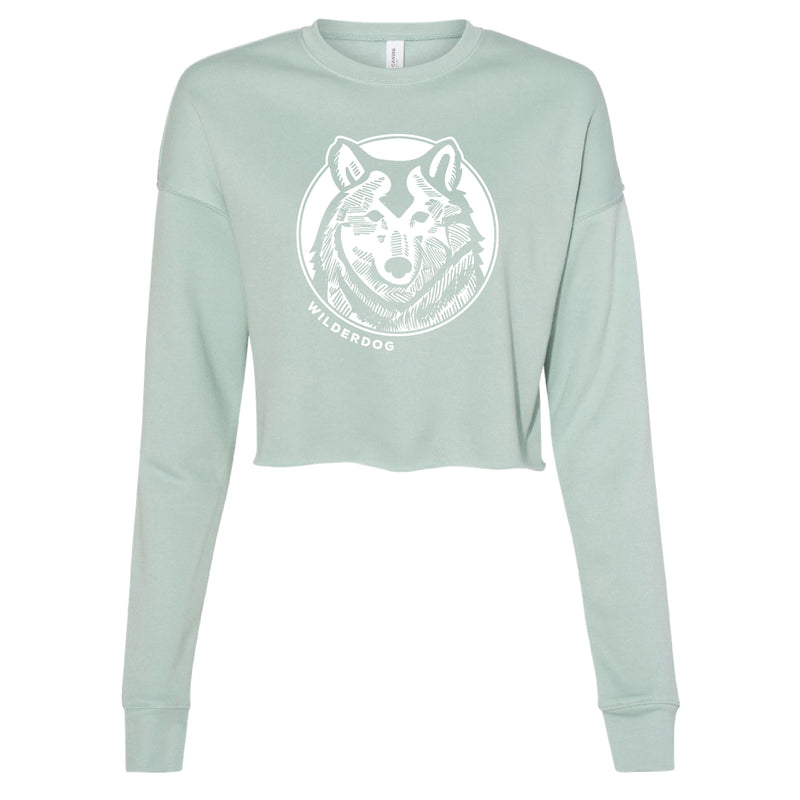 The Wilderdog Wolf Cropped Sweatshirt is a light green women's top featuring a large white graphic of a wolf's head in the center, with the text "WILDERDOG" printed below. Made from super-soft fleece, this eco-friendly sweatshirt offers long sleeves and a crew neck for ultimate comfort and style.